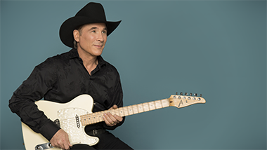 clint black sitting with a white guitar against a turquoise background