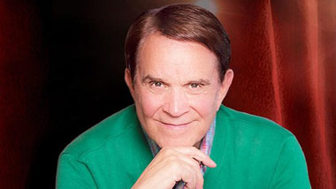 Rich Little with red curtain behind him